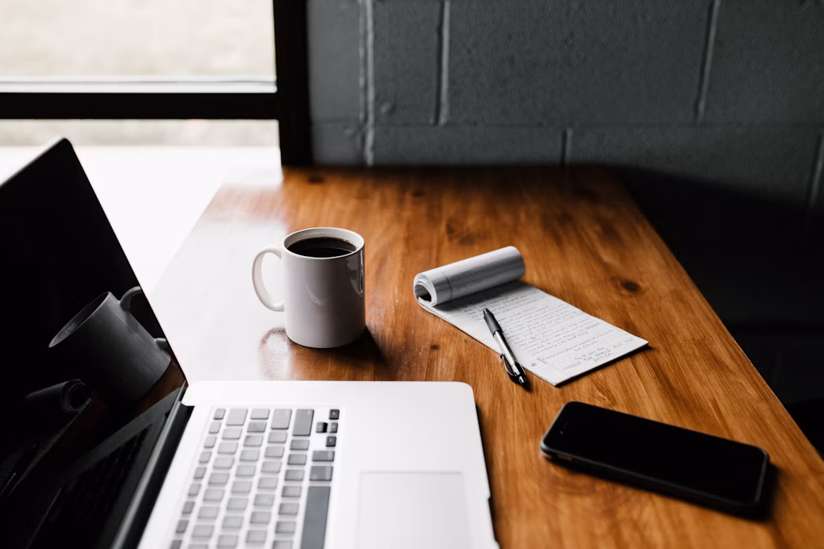 A developer's workspace with a laptop, notebook and coffee on a wooden desk